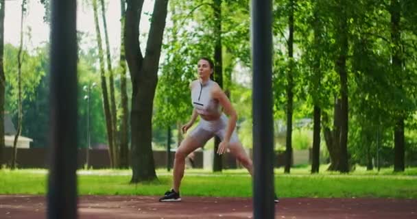 La atleta realiza embestidas laterales, resuelve sus piernas y salta en el parque en cámara lenta. Hermosa mujer practicando deportes en el Parque . — Vídeo de stock