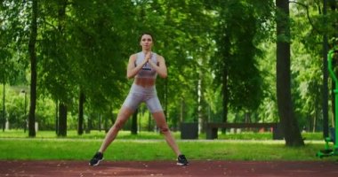 Dişi sporcu yan hamleler yapıyor. Parkta bacaklarını yavaş çekimde çalıştırıyor. Parkta spor yapan güzel bir kadın..