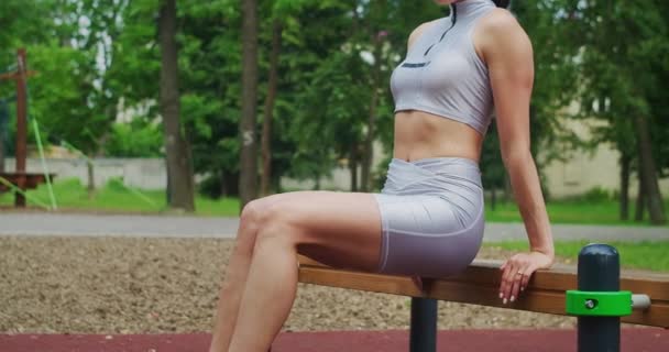A female athlete performs reverse exercises on a bench in a Park in slow motion. Beautiful woman playing sports in the Park — Stock Video