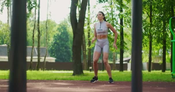 Female athlete performs side lunges work out her legs and jumping in the Park in slow motion. Beautiful woman playing sports in the Park. — Stock Video