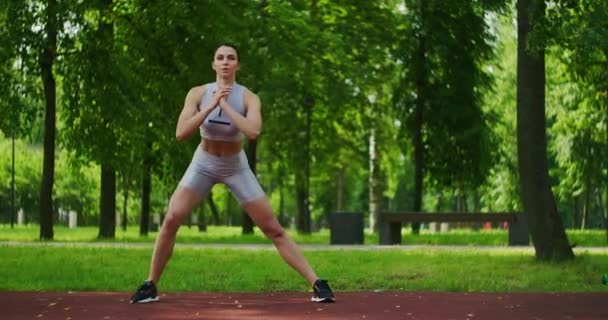 Atleta feminina executa lunges laterais exercitar suas pernas no Parque em câmera lenta. Mulher bonita jogando esportes no parque . — Vídeo de Stock