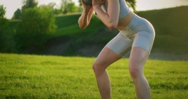 Gün batımında dambıllarla parkta çömelmiş bir kadın yan tarafa doğru hamle yapıyor. Motivasyon ve spor eğitimi. Bekar bir kadın yazın gün batımında egzersiz yapar.