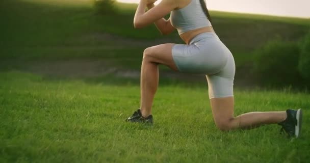 La caméra suit une athlète féminine se balançant par paires au coucher du soleil. Déplacez-vous en vous accroupissant sur chaque jambe à son tour — Video