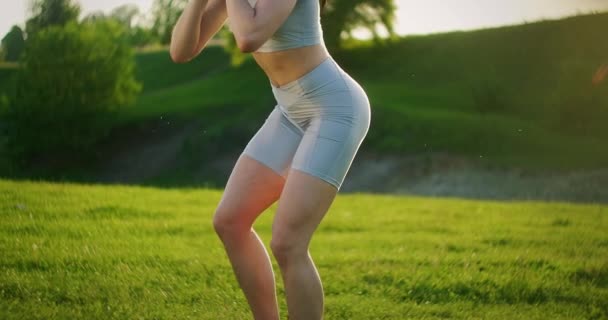 Une femme accroupie avec des haltères dans le parc au coucher du soleil se jette sur le côté. Motivation et entraînement sportif. Une femme célibataire fait des exercices au coucher du soleil en été — Video