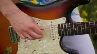 Kameranın manuel hareketi dans eden gitaristi takip ediyor. Tişörtlü bir adam, kolza tarlasında gitar çalıyor..