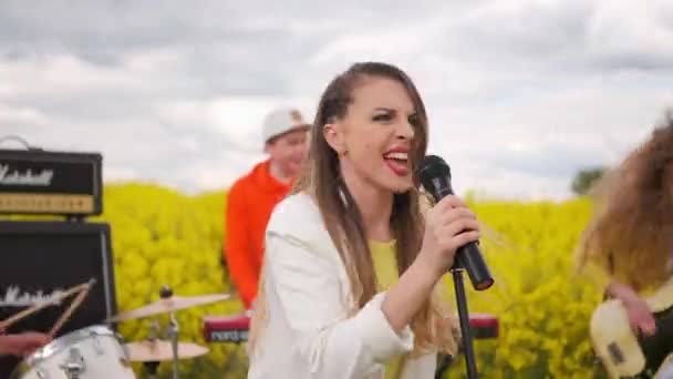 Un gruppo musicale suona in un campo di fiori gialli. Il solista canta nel microfono. Musica energica e danza. Suona strumenti musicali — Video Stock