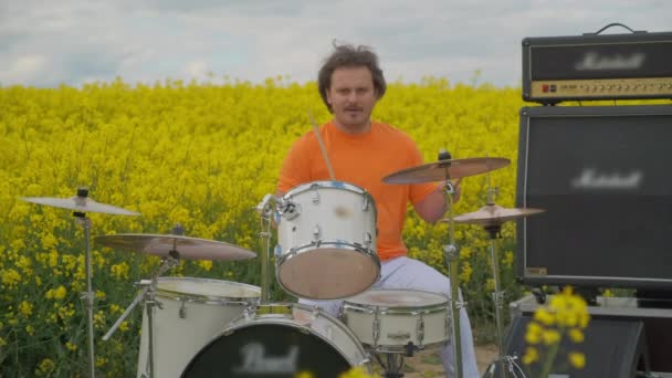 Perkusista w polu kwiatów gra na instrumentach — Wideo stockowe