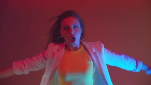 Une jeune femme incendiaire danse chante et regarde la caméra à la lumière de projecteurs néons colorés et de lumières clignotantes — Video