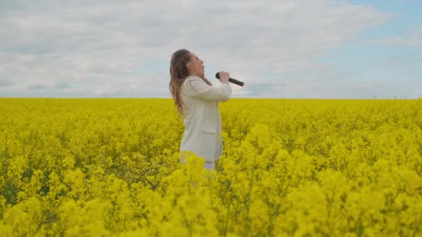 Hermosa chica cantante en un campo amarillo bailando y energizante mirando a la cámara — Vídeos de Stock