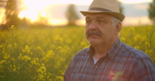 Un fermier en chapeau regarde la caméra et sourit. Le conducteur du tracteur regarde la caméra et sourit. Portrait d'un agriculteur âgé. — Video