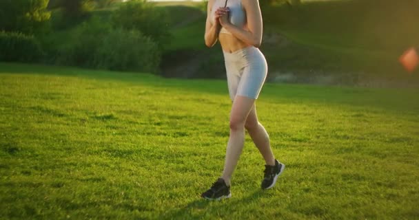 Жінка вистрибує і змінює ноги в свою чергу, тренуючи стегна і сідниці. Навчання жінок у парку на заході сонця — стокове відео