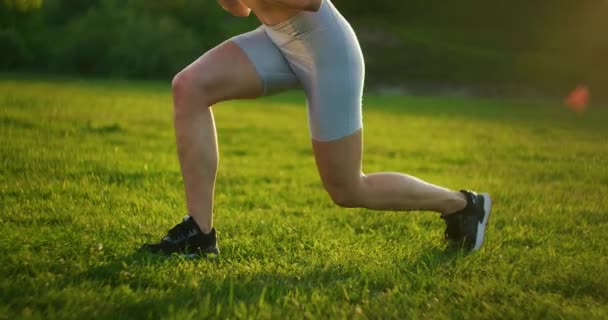 Žena vyskočí a střídavě si změní nohy tréninkem stehen a hýždí. Školení žen v parku při západu slunce — Stock video