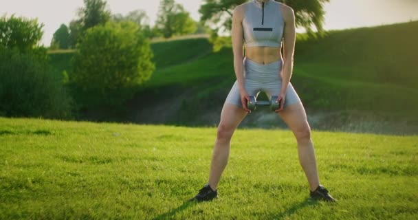 Strong sportswoman performs exercises for muscles of thighs and buttocks outdoors — Stock Video