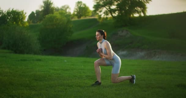 Cardio tränar kvinnor i parken. En ung vacker kvinna hoppar och byter ben i parken vid solnedgången.. — Stockvideo