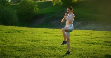 Bir kadın parkta antrenman yaparken hamle yapar ve bacağını dizinden kaldırır.