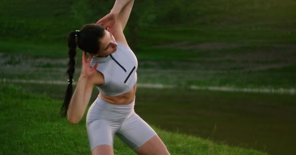 Un ritratto di una donna esegue esercizi per i muscoli della stampa. Allenamento sportivo nel parco di un bellissimo atleta slanciato al tramonto — Video Stock