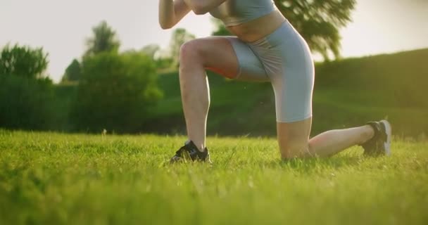 La cámara observa a la mujer levantando las piernas y haciendo retrocesos durante una sesión de entrenamiento en el parque — Vídeos de Stock