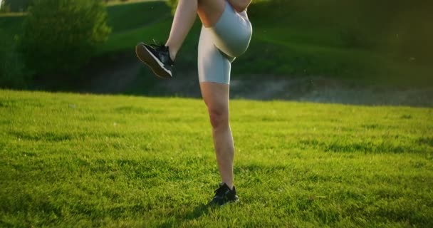 Un primer plano de una mujer joven realiza embestidas inversas en un parque en la hierba. Deportiva. Entrenamiento — Vídeos de Stock