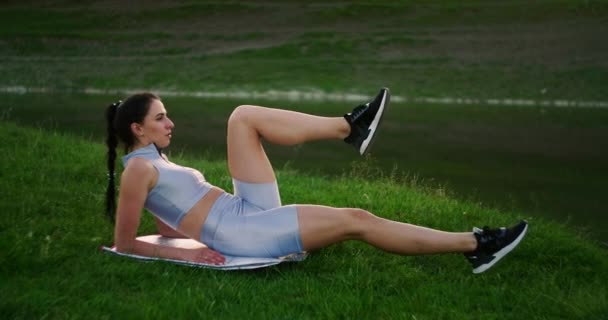 Le matin, dans le parc, une femme en tenue de sport allongée sur un tapis lève les jambes vers le vélo d'appartement du corps. Exercices pour un corps magnifique. Les muscles abdominaux — Video