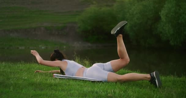 På morgonen i parken lyfter en kvinna i sportkläder på magen armarna och benen i tur och ordning. Övningar för en vacker kropp. Muskelstabilisatorer — Stockvideo