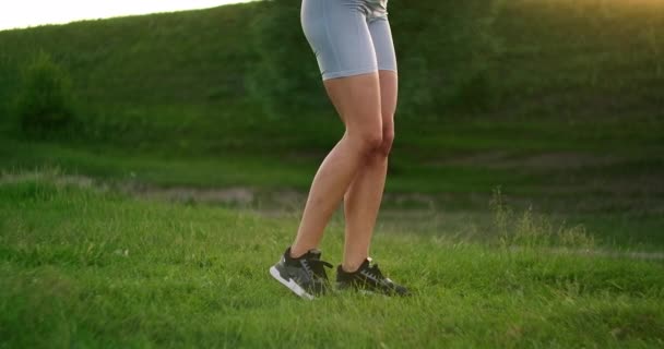 Lungor i sidan. En kvinna tränar för musklerna i låren och benen på gräset i en park nära sjön. Arbeta med magmuskler. Smal, vacker figur. Maraton om lämplighet — Stockvideo
