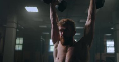 Spor salonunda dambılları kafasına doğru iten bir adamın portresi. Dayanıklılık, kol ve omuz kasları eğitimi