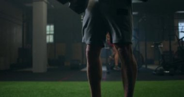 Elinde dambıl tutan güçlü bir adam spor salonunda viraj yapıyor. Sıkı bir egzersizden terleyen bir adam, dambıllarıyla egzersiz yapar. sağlıklı yaşam tarzı ve vücut geliştirme