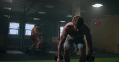 Performans çağından kalma güçlü, kaslı bir adamın, spor salonundaki dambıllarla ağırlık kaldırma egzersizinin ellerinde bükülmeleri..