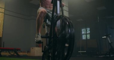 Bir adam spor salonunda ağır çekimde aerobik yapıyor. Sabit bir bisiklette kardiyo eğitimi