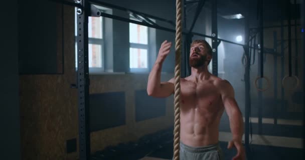 Un hombre fuerte bombeado en el gimnasio sube la cuerda y llega a la cima — Vídeo de stock