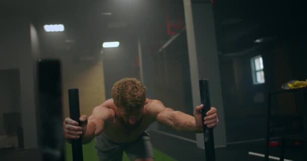 Um tenaz atleta solteiro empurra um trenó pesado no ginásio. exercício com um peso pesado para resistência — Vídeo de Stock
