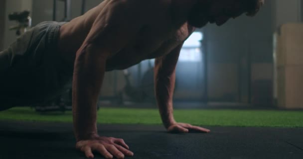 Ein starker Mann führt mit aller Kraft Liegestütze vom Boden aus aus aus. Ein aufgepumpter Mann macht Liegestütze im Fitnessstudio — Stockvideo