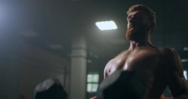 Güçlü ve güçlü bir atlet, spor salonunda ağır çekimde duran dambılları itiyor..
