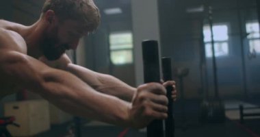 Ağır çekimde spor salonunda kaslı bir adam kızağı itiyor.