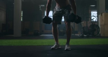 Sportif ve şişkin erkek, spor salonunda dambıllarla sırt kaldırma egzersizleri yapıyor.