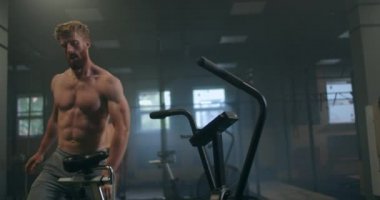 Bir adam spor salonunda ağır çekimde aerobik yapıyor. Sabit bir bisiklette kardiyo eğitimi