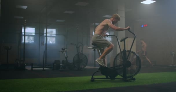 Een man domineert een aerobics rit in de sportschool in slow motion. cardiotraining op een stationaire fiets — Stockvideo