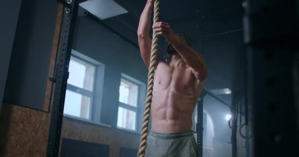 Un hombre en el gimnasio sube la cuerda a la cima. perseverancia y fuerza. un hombre sudoroso sin camiseta está entrenando . — Vídeos de Stock