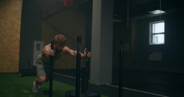 Мускулистый мужчина толкает сани в тренажерном зале во время замедленных упражнений — стоковое видео