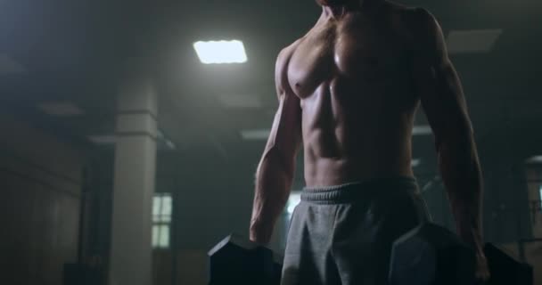 En stark man håller hantlar i händerna utför böjar i gymmet. svettas efter hård träning, utför en man övningar med hantlar. hälsosam livsstil och bodybuilding — Stockvideo