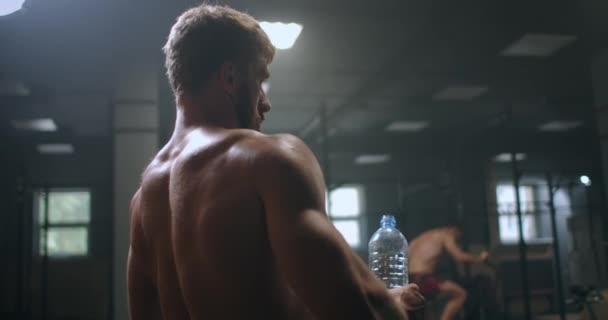 Ein athletischer Mann trinkt Wodka, um nach und vor einer Übung im Fitnessstudio wieder Kraft zu tanken. Trinken Sie während des Trainings Wasser aus der Flasche — Stockvideo