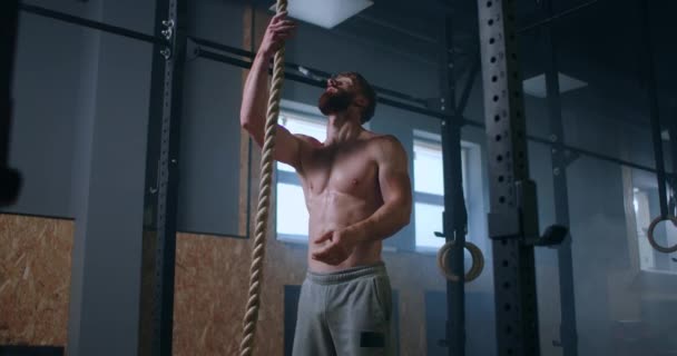Een man in de sportschool klimt het touw naar de top. doorzettingsvermogen en kracht. een zweterige man zonder t-shirt traint. — Stockvideo