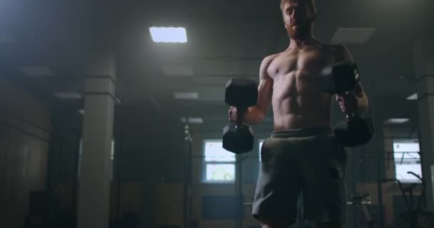 A strong man from the years raises dumbbells in the gym. to perform the exercises with dumbbells. the concept of endurance, determination, and goal achievement — Stock Video