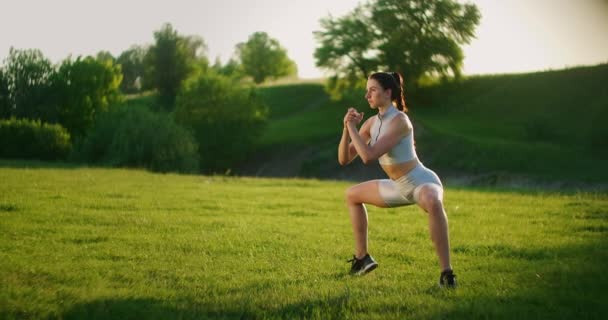 Mladá žena provádí statické cvičení na trávě pro stehenní a kyčelní svaly. Postavit se na špičky, když sedím. Cvičení na dolní končetinu. Školení na ulici v parku — Stock video