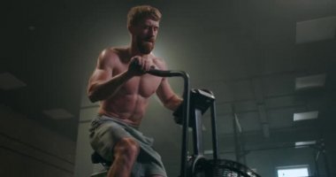 Bisikletli fitness adamı spor salonunda dönüyor. Spor bisikletinde spor yapan formda genç bir erkek. Sağlık kulübünde bisiklete binen bir erkek.