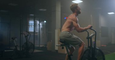 Genç adam spor salonunda egzersiz bisikleti kullanıyor. Fitness erkeği spor salonunda hava bisikleti kullanıyor. Ekipman, çaba.