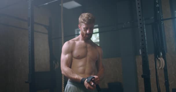 Young athletic Caucasian man changing, putting weight lifting straps on in gym locker room before workout slow motion. ties arms to barbell with fitness straps. — Stock Video