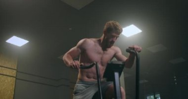 Bisikletli fitness adamı spor salonunda dönüyor. Spor bisikletinde spor yapan formda genç bir erkek. Sağlık kulübünde bisiklete binen bir erkek.