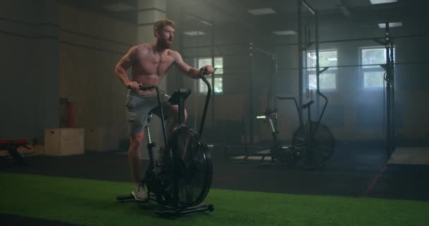Чоловік займається фізичними вправами на велосипеді тренажерний зал фітнес. Фітнес-чоловік з використанням кардіо-тренувань на повітряному велосипеді. Спортсменка використовує тренажери в сучасному темному тренажерному залі . — стокове відео