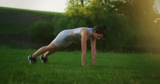 草の上の公園の女性が板の運動に立ち右手と左手を順番に上げていきます。腹筋に静的運動 — ストック動画